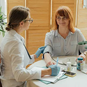 Healthcare professional wearing gloves taking a blood sample from a smiling woman during a medical consultation in a clinic